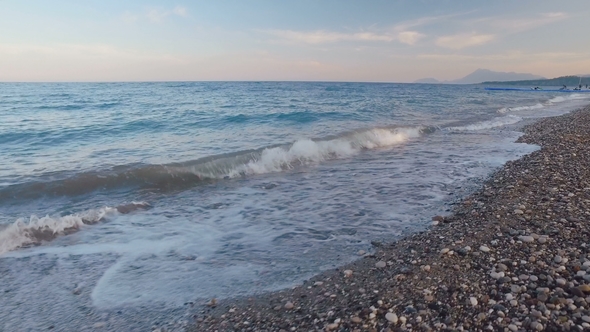 Camera Moves Parallel Pebble Seashore, Blue Waves in Twilight, Mountains Are in Background