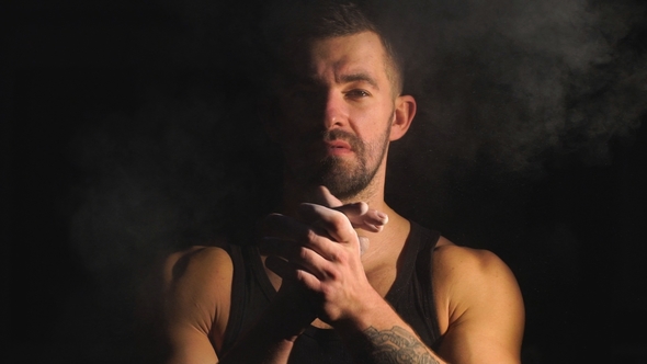 Strong Muscular Bearded Bodybuilder Clapping Hands with Chalk Powder Before Training with a Dumbbell