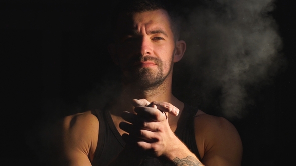 Strong Muscular Bearded Bodybuilder Clapping Hands with Chalk Powder Before Training with a Dumbbell