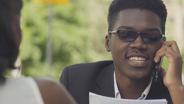 Young Positive Afro American Entrepreneur in Trendy Eyewear Having Phone Conversation with Secretary alt