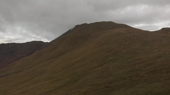 Advance drone shot of green grass mountain top in loch lomond national park in scotland during cloud alt