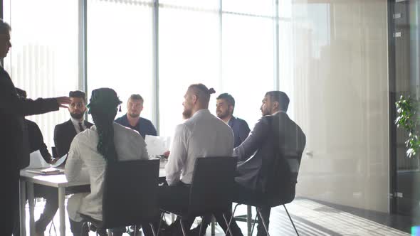 Multiracial Male Business Executives Discuss Project Sitting at Conference Table alt