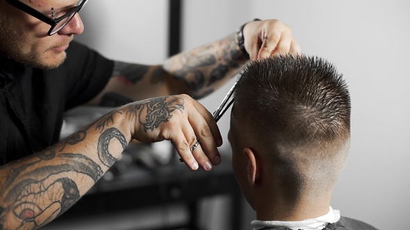 Tattoed Barber Makes Haircut for Customer at the Barber Shop By Using Scissors and Comb , Man's