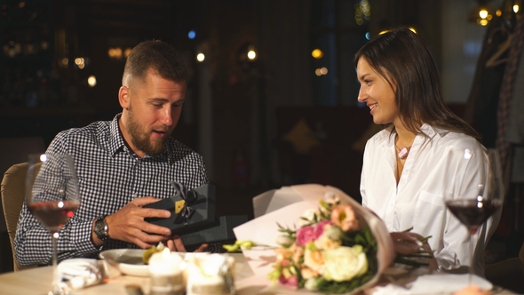 A Beautiful Brunette Girl Gives a Gift To Her Boyfriend in a Restaurant on a Date