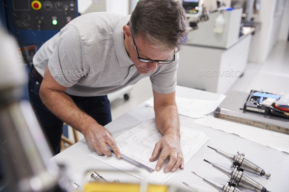Male Engineer Measuring CAD Drawings In Factory Stock Photo by monkeybusiness