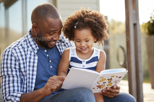 Young black father and daughter reading book outside Stock Photo by monkeybusiness