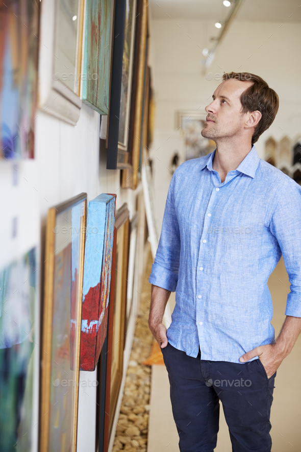 Man Looking At Paintings In Art Gallery Stock Photo by monkeybusiness