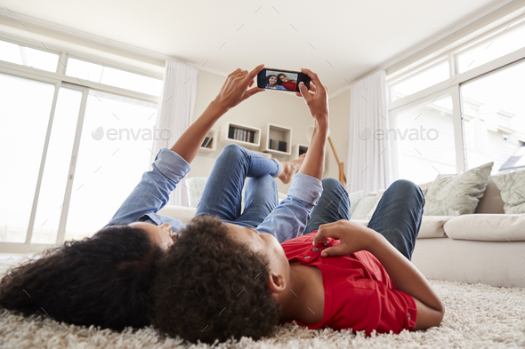 Mother And Son Lying On Rug And Posing For Selfie At Home Stock Photo by monkeybusiness