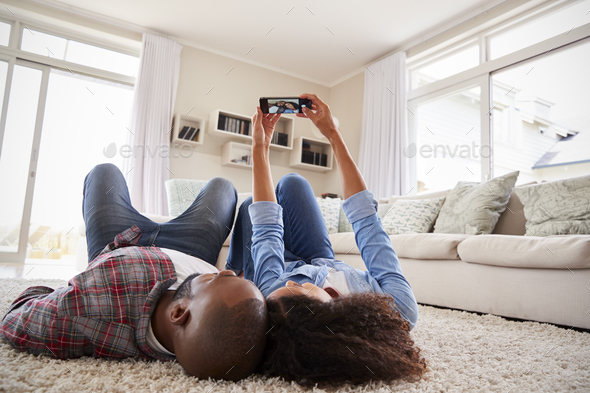 Couple Lying On Rug And Posing For Selfie At Home Stock Photo by monkeybusiness