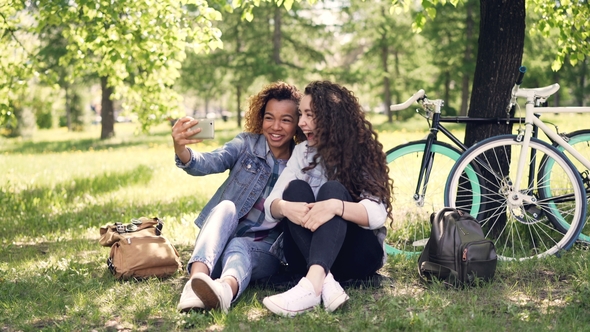 Cheerful Women Are Looking at Smartphone Screen and Laughing Then Taking Selfie Together Posing for alt