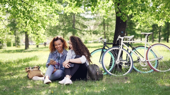 Happy African American Woman Is Showing Her Caucasian Friend Her Smartphone Screen alt