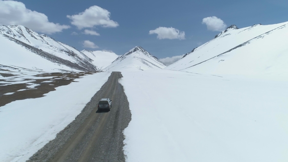 SUV Vehicle Goes on Road in Snowy Mountains at Sunny Day. Aerial View alt