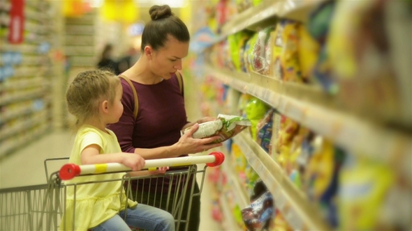 Mother and Daughter Shopping in Supermarket. They Are Buying a Breakfast Flakes. A Daughter Sitting alt