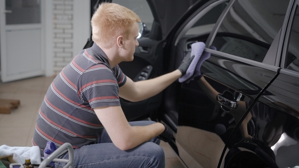 Worker Is Wiping Doors of Luxury Black Car After Protective Processing and Washing in a Garage alt