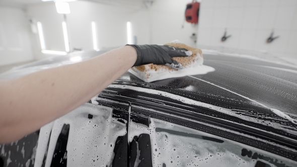 Washerman Is Rubbing Surface of Black Automobile By Sponge with Soap Foam in Car Washing, Wearing alt