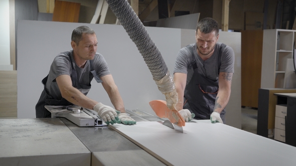 Two Joiners Are Directing Wooden Board on Industrial Sawing Machine in Furniture Factory, Cutting of alt