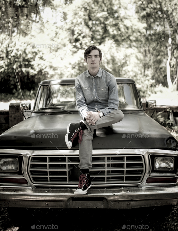 Portrait of young man sitting on old pickup truck - Stock Photo - Images