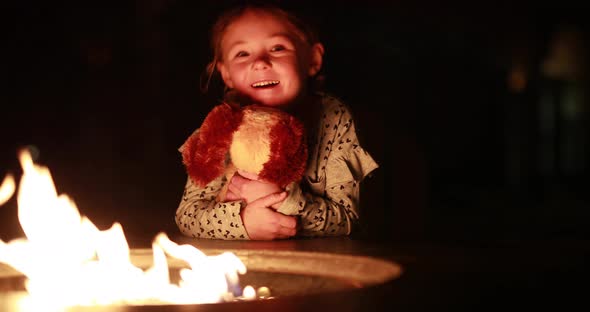 A young girl enjoys a fire with her stuffed animal puppy. alt
