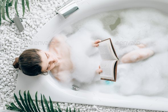 Woman lying in bath with foam and reads magazine Stock Photo by NomadSoul1