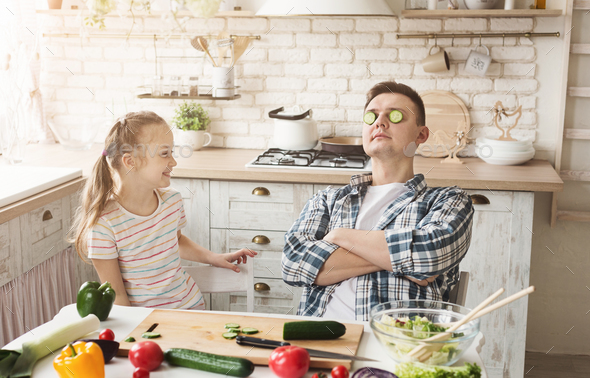 Little girl and dad having fun while cooking in kitchen Stock Photo by Prostock-studio