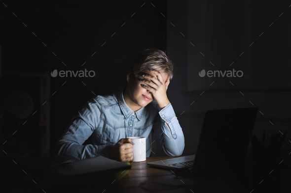 Tired woman with laptop at dark home office copy space Stock Photo by Prostock-studio