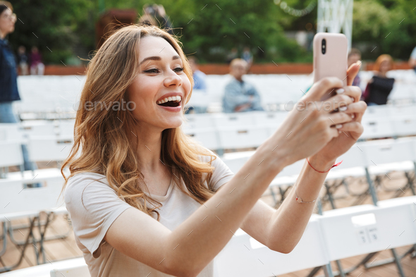 Smiling young girl taking picture with mobile phone Stock Photo by vadymvdrobot