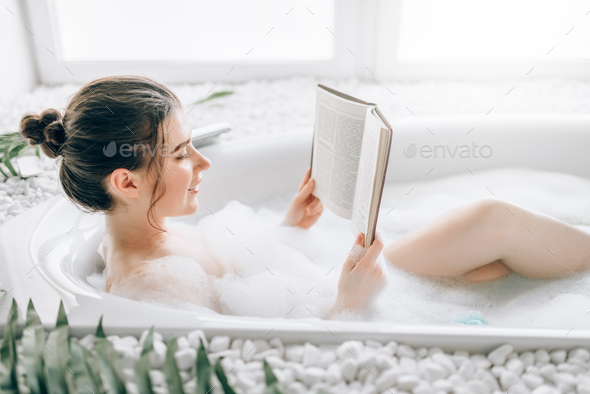 Woman lying in bath with foam and reads magazine Stock Photo by NomadSoul1