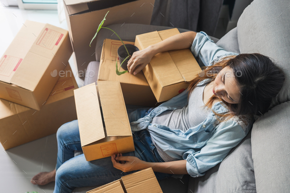 Young tried woman moving in new home, sitting and relaxing on sofa Stock Photo by kitzstocker
