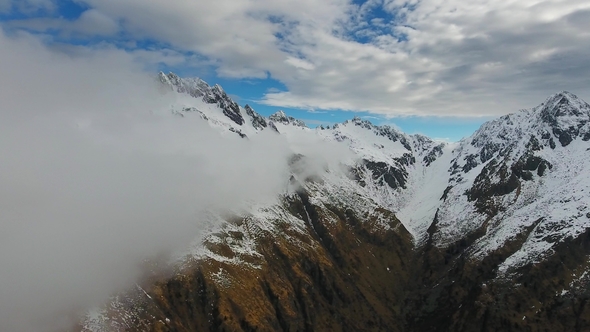 Flying in Clouds Between Snow-capped Mountains alt