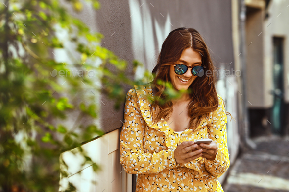 Smiling woman sitting in the city reading a text message Stock Photo by UberImages