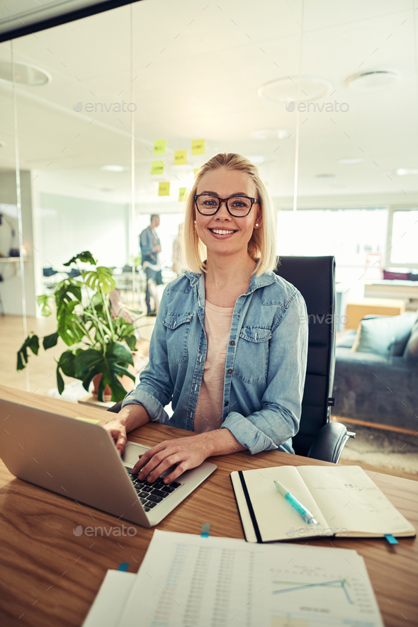 Young businesswoman smiling confidently while sitting at her office desk - Stock Photo - Images