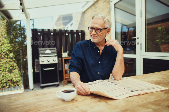 Smiling senior man relaxing on his patio reading the newspaper Stock Photo by UberImages