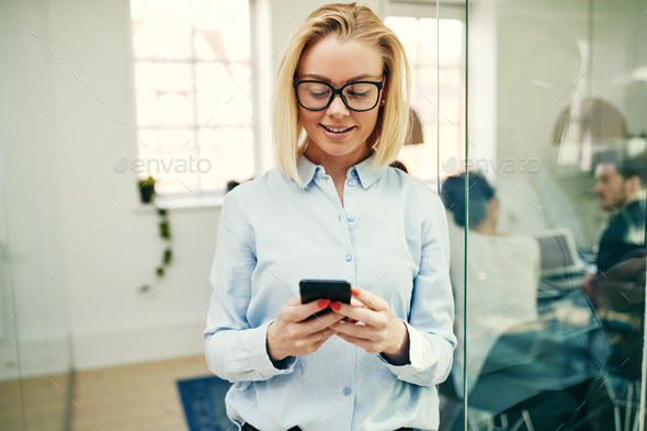 Smiling businesswoman standing in an office sending a text message - Stock Photo - Images