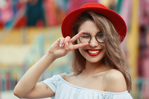 Cheerful girl winking and smiling while showing victory sign - Stock Photo - Images