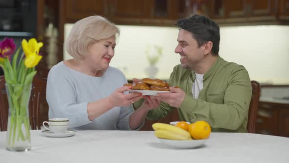 Grateful Adult Son Hugging Senior Mother Smiling Talking Thanking for Delicious Baked Dessert alt