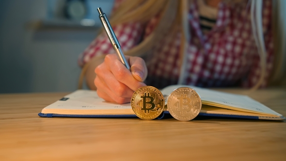 Woman Writing in Notebook with Bitcoins Nearby Crop View of Female Hands in Checkered Shirt Holding alt
