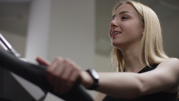 Blonde Girl Turns the Pedals on an Exercise Bike, Watch the Tv with Training Stream in New Gym