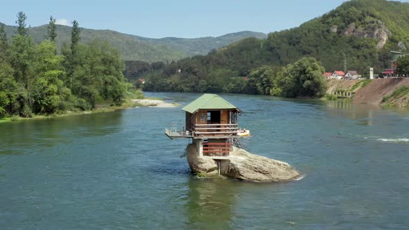 Drone Video in Which a Small House Stands on a Rock in the Middle of the River alt