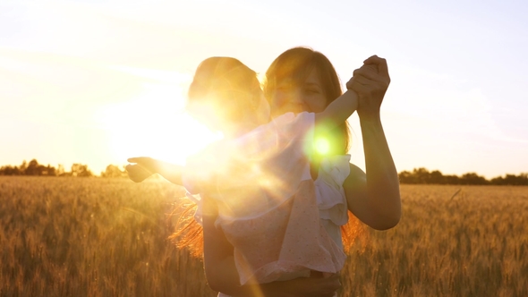 Young Mother with a Small Baby Dancing and Laughs Against the Backdrop of a Golden Sunset in a Field alt