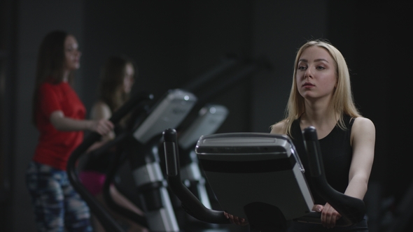 Cute Blonde Girl Is Diligent Working on an Exercise Bike and Cool Guy Come To Her