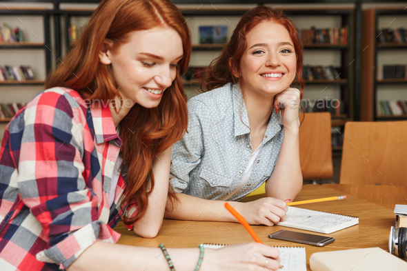 Portrait of a two happy teenage girls doing homework Stock Photo by vadymvdrobot