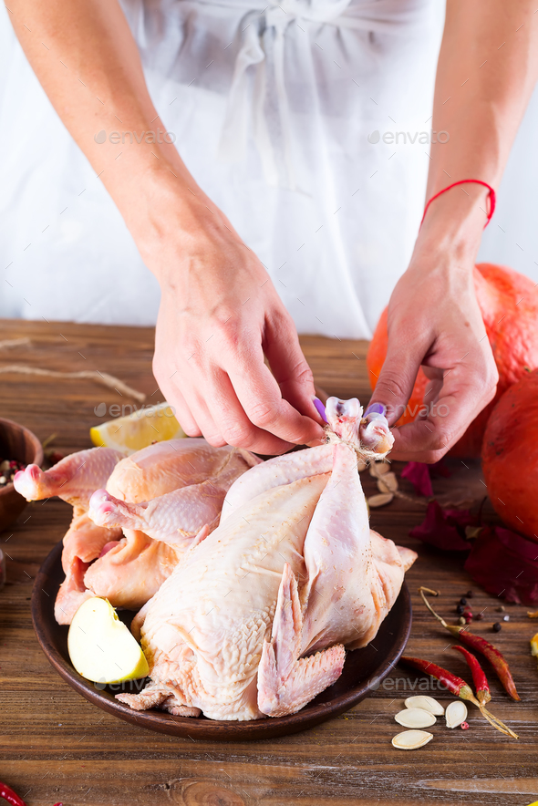 Raw whole chicken in a plate on a wooden table. The woman\'s hands prepare the chicken for frying. Stock Photo by lyulkamazur