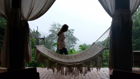 A young asian woman sitting and relaxing on hammock while looking at a beautiful nature view