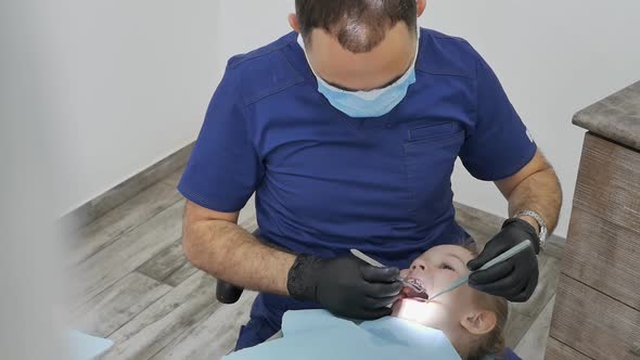 a Middle Eastern Male Pediatric Dentist Fills the Tooth of a Caucasoid Little Girl Lying with Her
