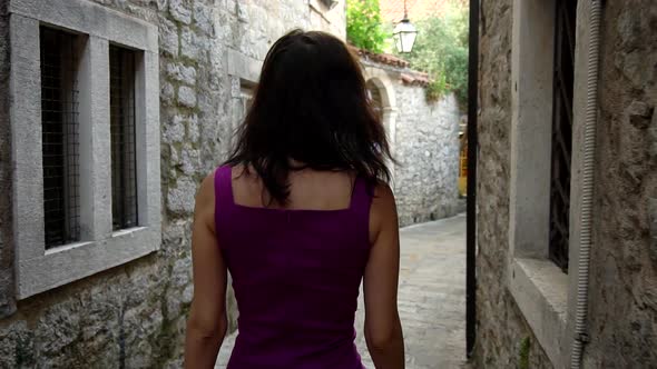 A Beautiful Brunette Girl Walks Along the Narrow Streets of the Old City and Looks at the Camera alt