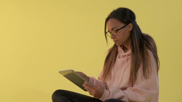 Black Woman in Eyeglasses Working on Tablet on Yellow Background alt