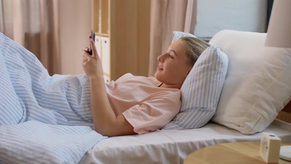 Happy Girl with Smartphone in Bed at Home alt