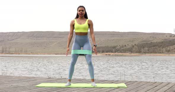 Motivated black woman doing exercises for legs with rubber stripe