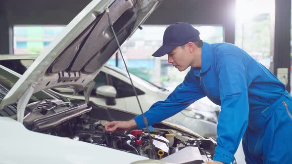 Asian automotive mechanic man open a car hood and check up the engine. alt