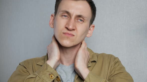 Tired Young Man Suffering Neck Pain While Standing on Gray Background alt